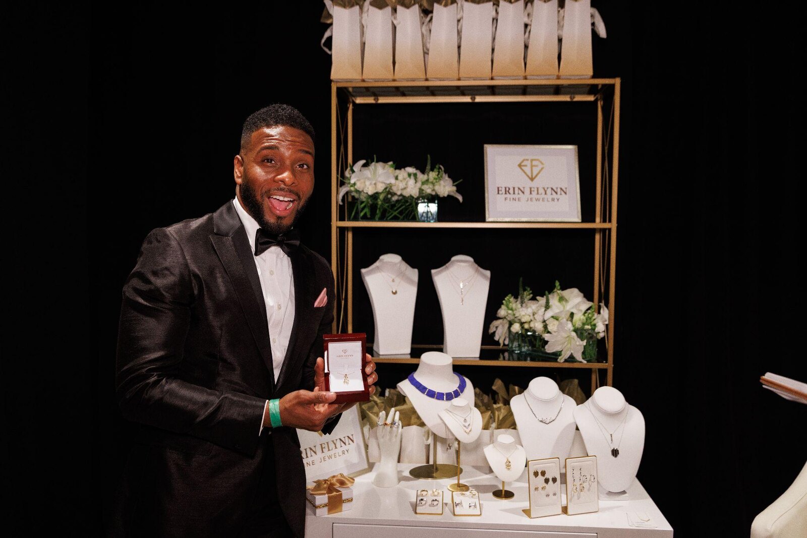 A guest in black tie holding an Erin Flynn Fine Jewelry gift box at the Emmys Giving Suite display
